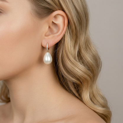 Close-up side view of a model with wavy blonde hair wearing an elegant 18k gold-plated huggie hoop earring with a dangling teardrop artificial pearl. The micro-pave cubic zirconia crystals on the hoop are clearly visible.