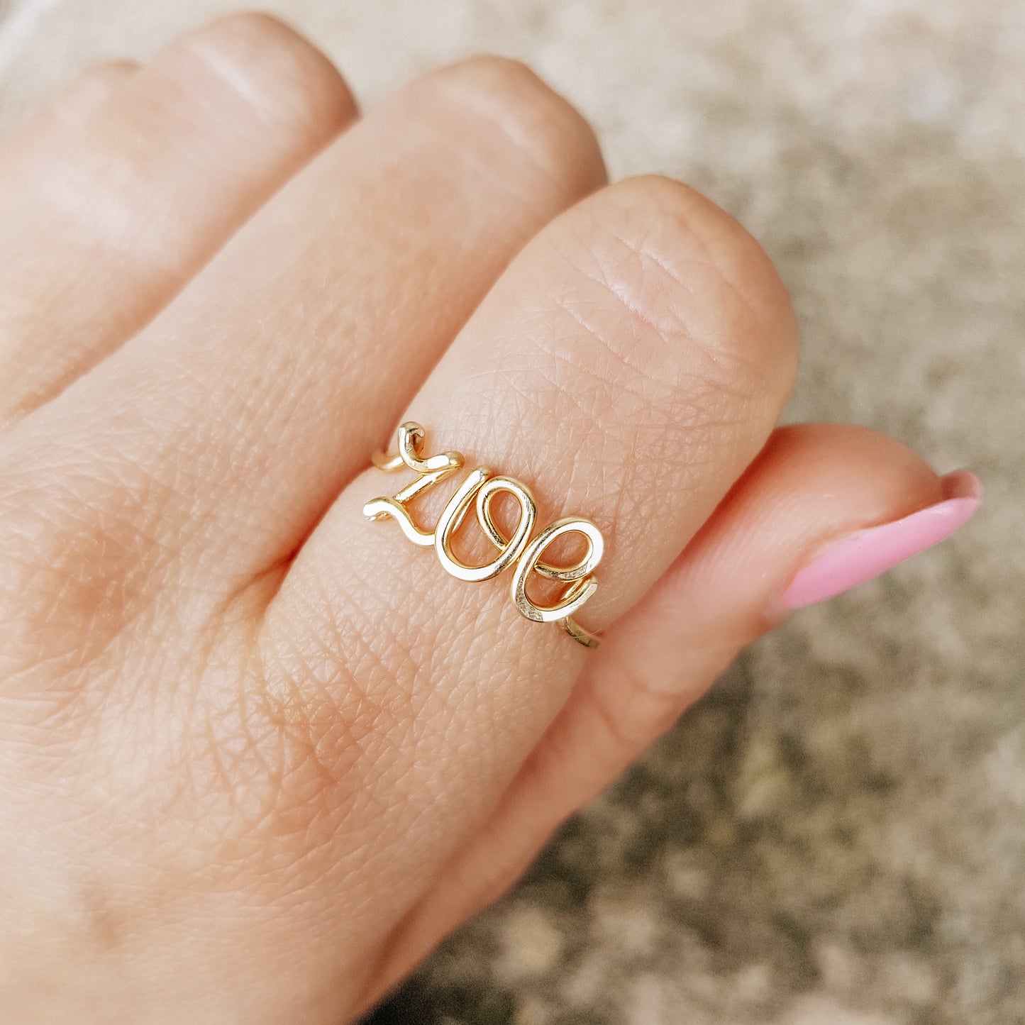 Handcrafted gold wire ring personalized with the name "Zoe" in cursive script, worn on a model's finger.