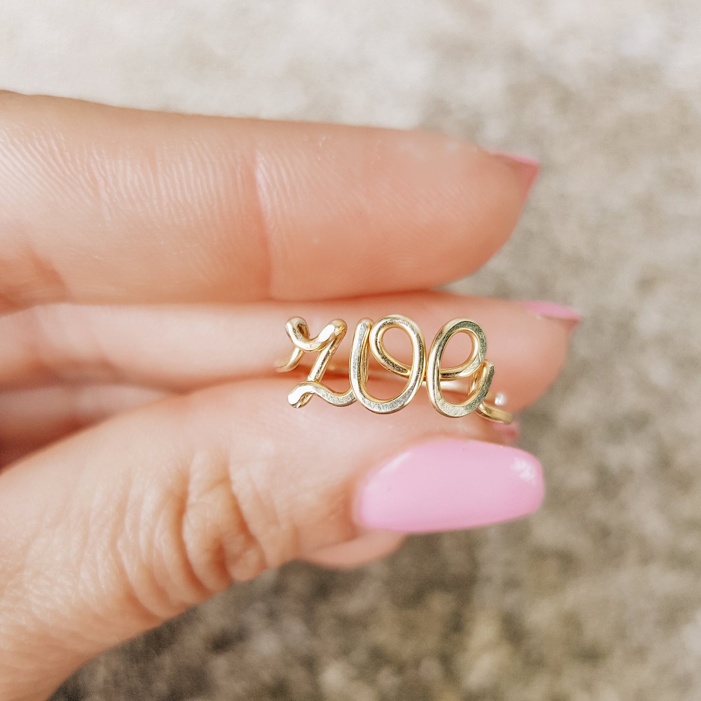 Handcrafted gold wire ring personalized with the name "Zoe" in cursive script, worn on a model's finger.