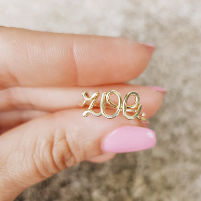 Handcrafted gold wire ring personalized with the name "Zoe" in cursive script, worn on a model's finger.