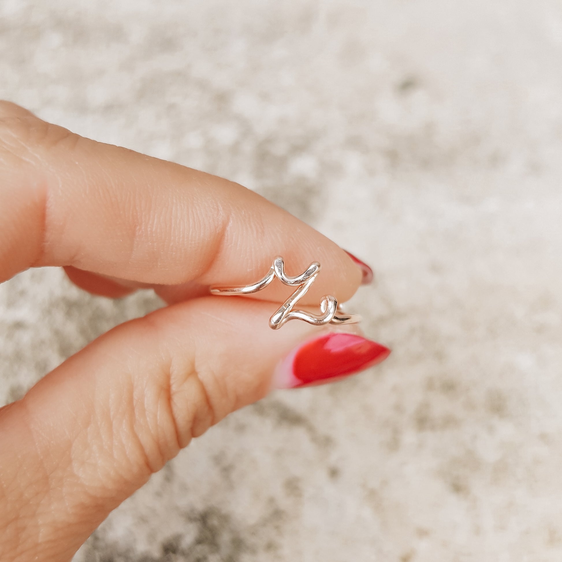 Handmade gold wire ring featuring a lowercase cursive letter Z, styled on a hand with elegant red french nails.