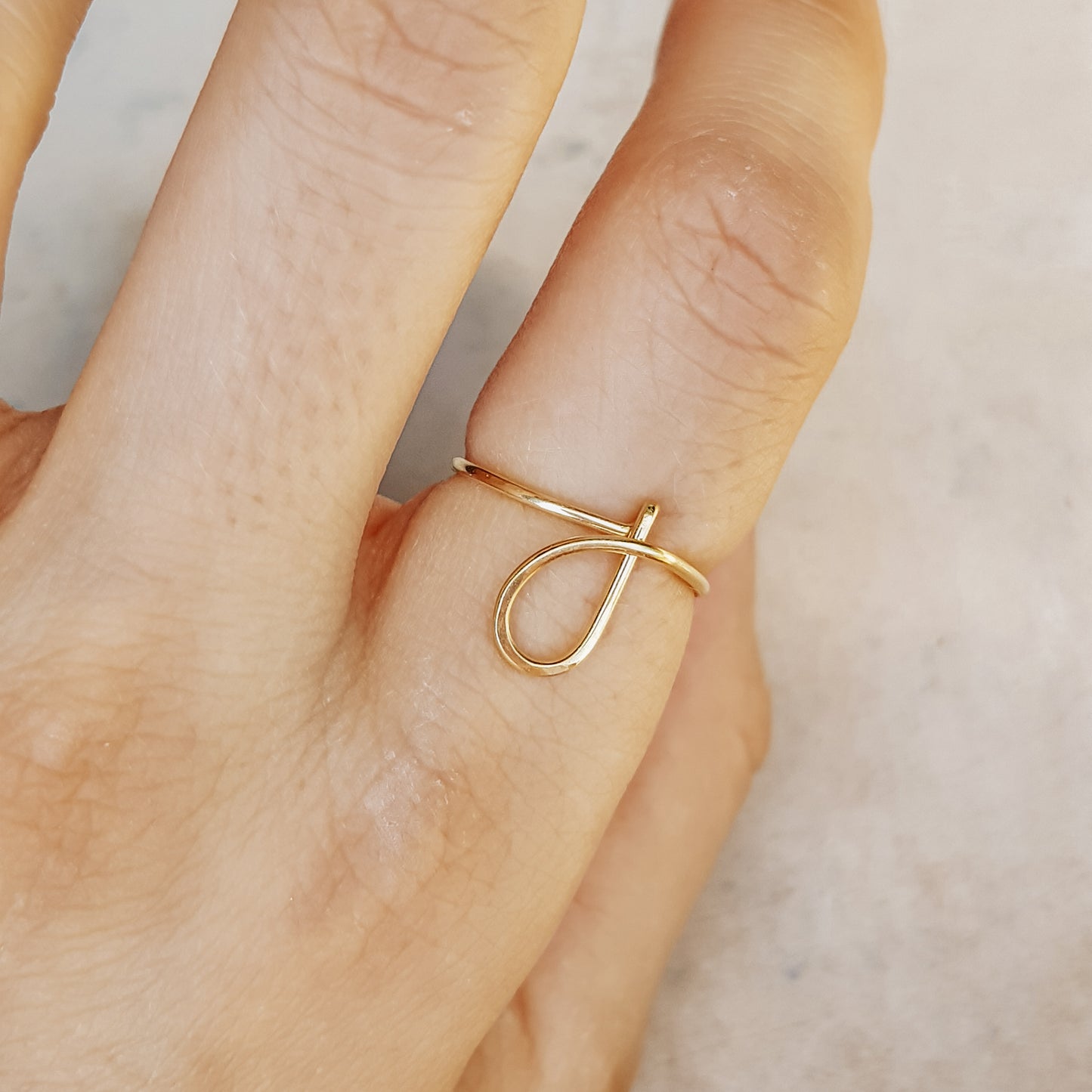 Close-up of a handmade 14k gold filled wire ring shaped into the letter J on a woman's finger.