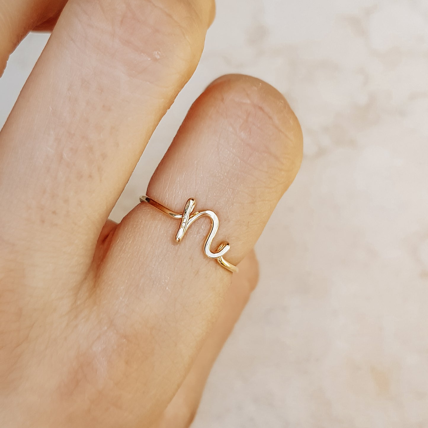 Close-up of a handmade 14k gold filled wire ring shaped into the letter N on a woman's finger.
