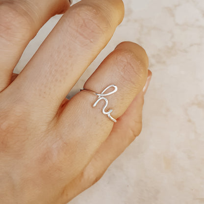 Close-up of a handmade 925 sterling silver wire ring shaped into the letter H on a woman's finger.