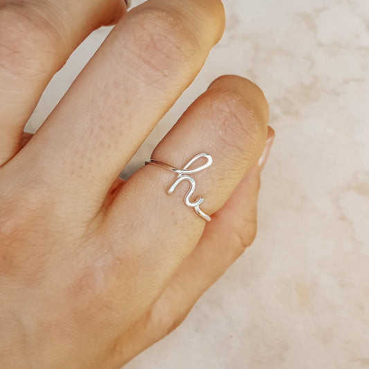 Close-up of a handmade 925 sterling silver wire ring shaped into the letter H on a woman's finger.
