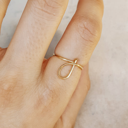 Handmade dainty gold wire ring with a lowercase cursive letter J design, worn on a hand.