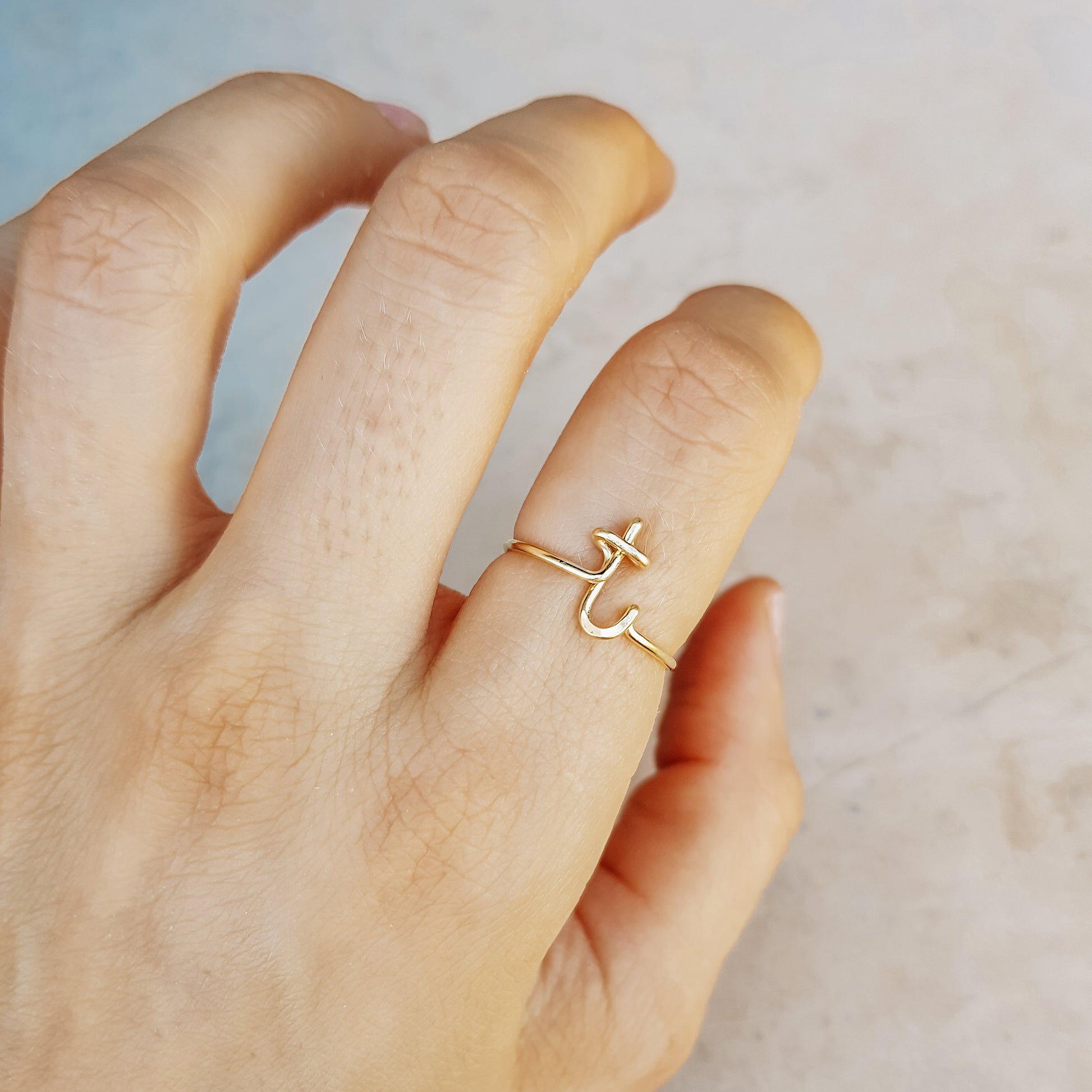 Close-up of a handmade 14k gold filled wire ring shaped into the letter T on a woman's finger.