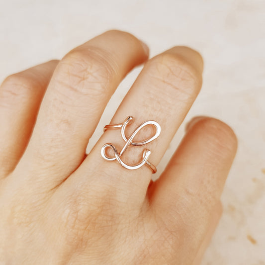 Elegant handmade rose gold wire ring with an uppercase cursive letter L, worn on a hand.