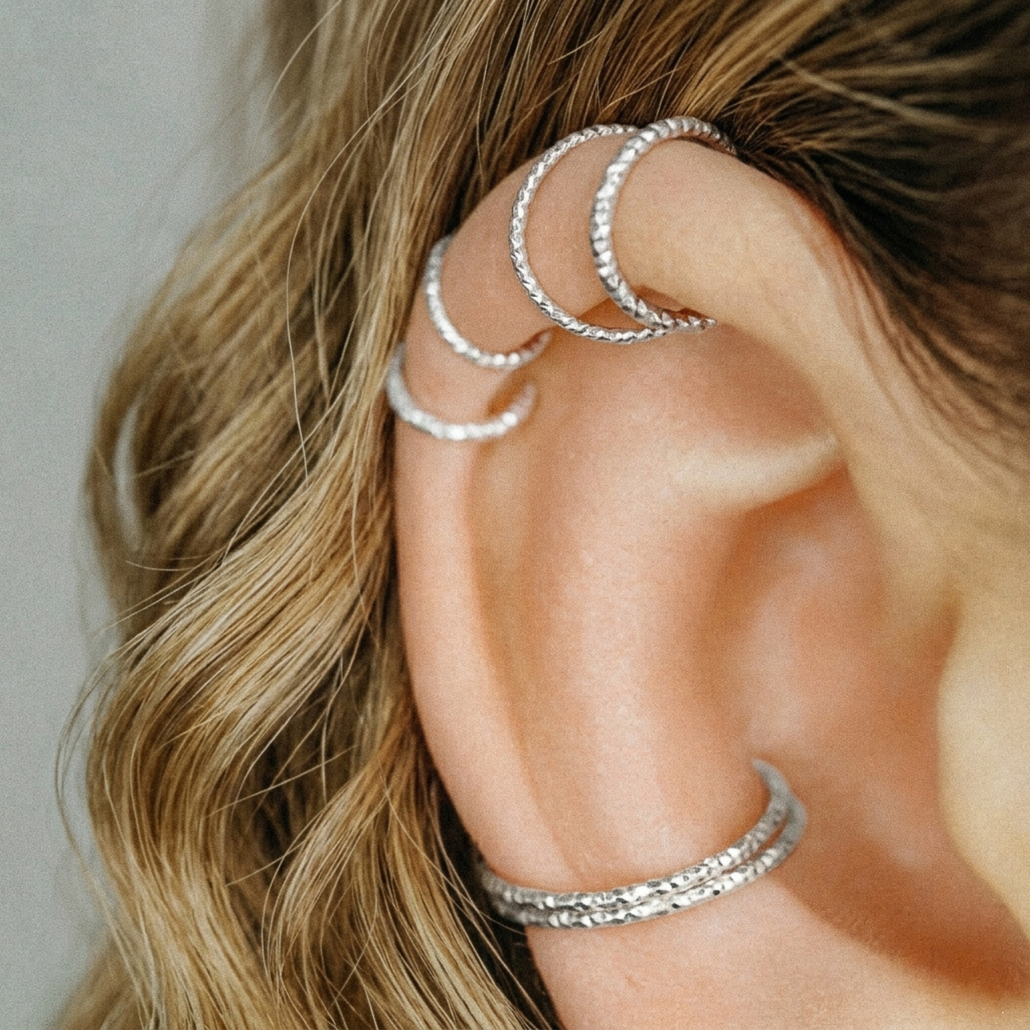 Close-up of three 925 Sterling Silver diamond-cut endless hoop earrings in a helix piercing.