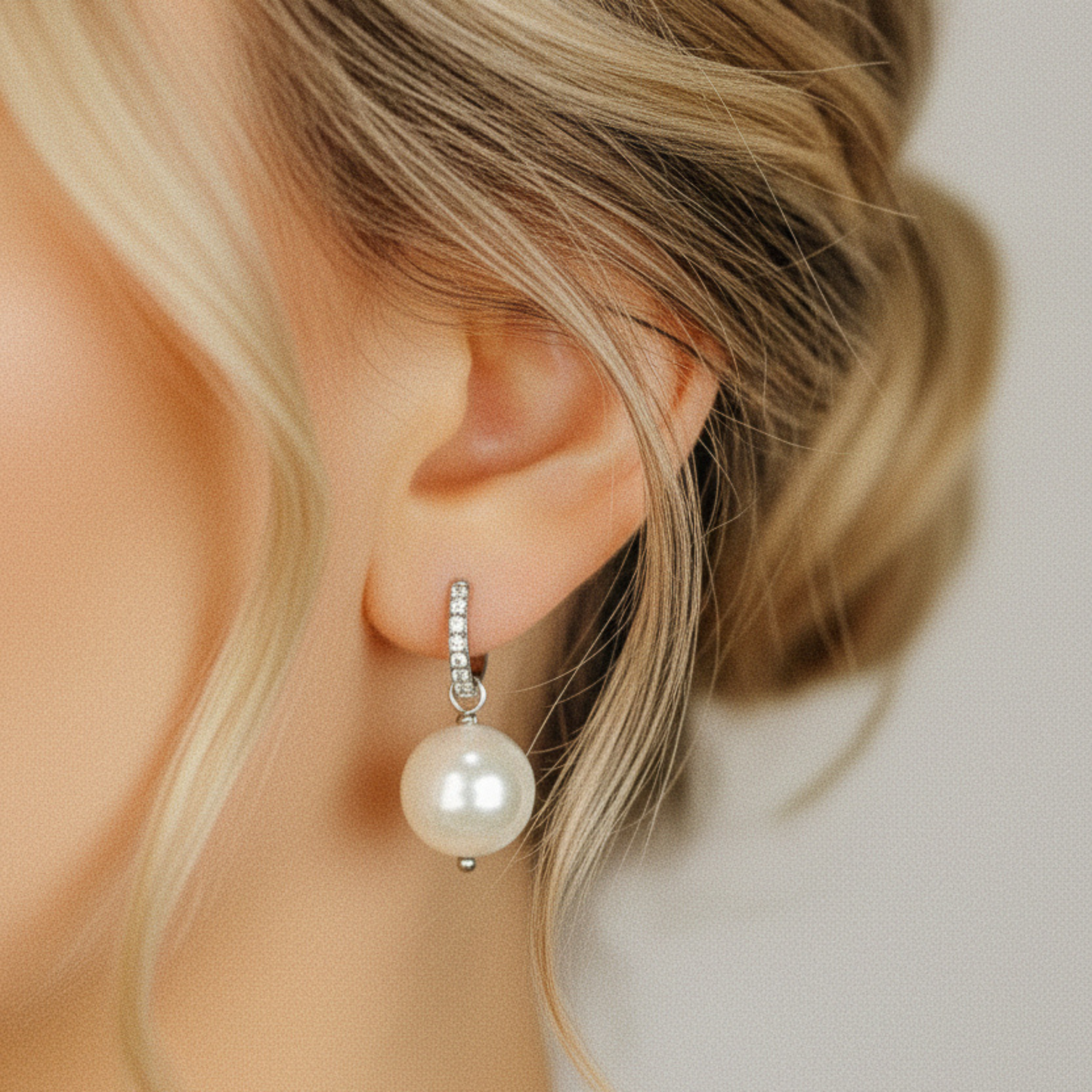 Close up of a woman wearing a 13mm ceramic pearl drop earring with 18k gold hoop finish.