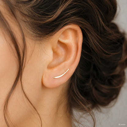 15 mm handmade hammered ear climber shown on the ear, designed as a dainty curved bar earring that follows the natural ear shape from the lobe upward. Minimalist ear sweep style with slim reflective wire, available in solid 925 sterling silver, 14k gold filled and 14k rose gold filled, sold as single left, single right or pair.