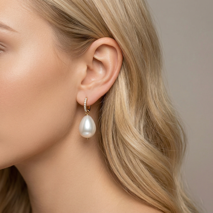 Angled lifestyle portrait of a woman wearing a polished gold hoop earring with a large lustrous artificial pearl drop. The tarnish-resistant 18k gold finish catches the light, perfect for bridal or formal wear.