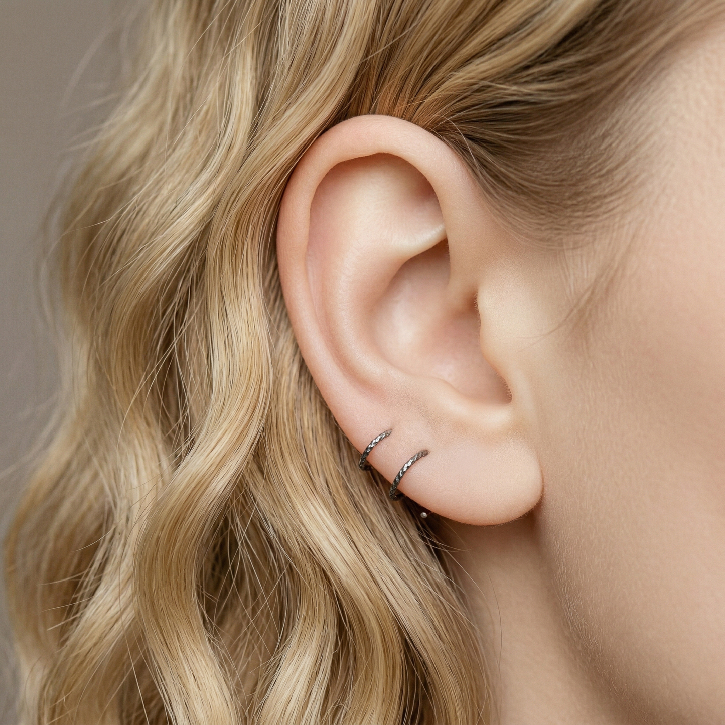 Minimal black double hoop spiral earrings worn on ear, tiny ruthenium sterling silver illusion hoops creating double piercing look, diamond cut texture close-up