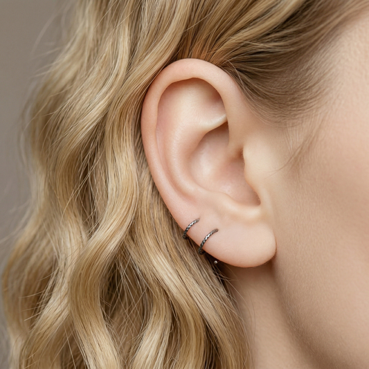 Minimal black double hoop spiral earrings worn on ear, tiny ruthenium sterling silver illusion hoops creating double piercing look, diamond cut texture close-up