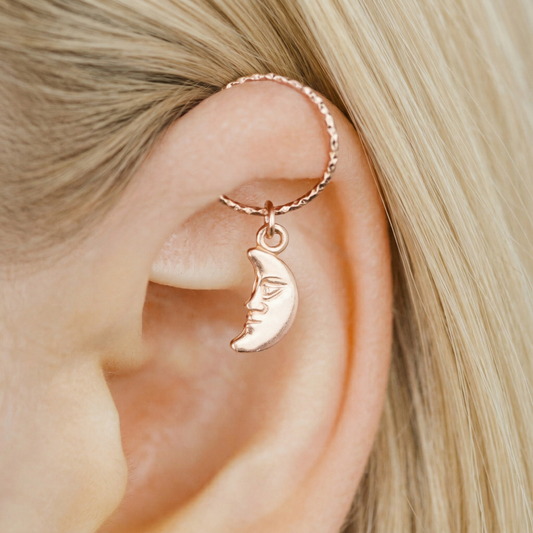 Close-up of a model wearing a rose gold diamond-cut helix hoop with a dangling crescent moon face charm.