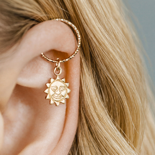 Close-up of a gold diamond-cut endless hoop earring with a smiling sun charm worn in a helix piercing.
