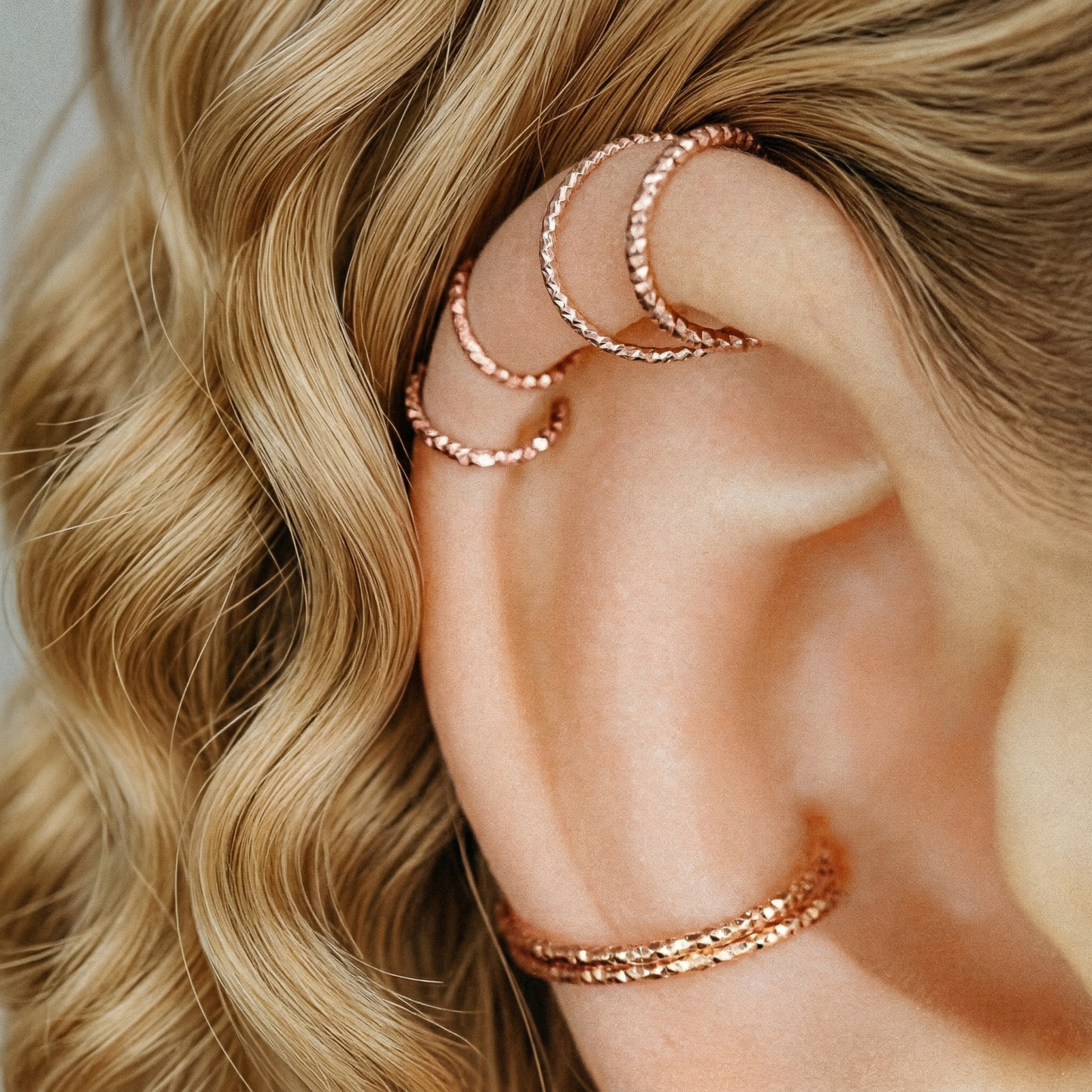 Multiple textured rose gold hoops styled in helix and lobe piercings for an ear party look.