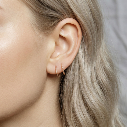 Close-up of a woman's ear wearing tiny rose gold double hoop illusion earrings with a diamond-cut texture, designed to create the appearance of two piercings with a single hole.