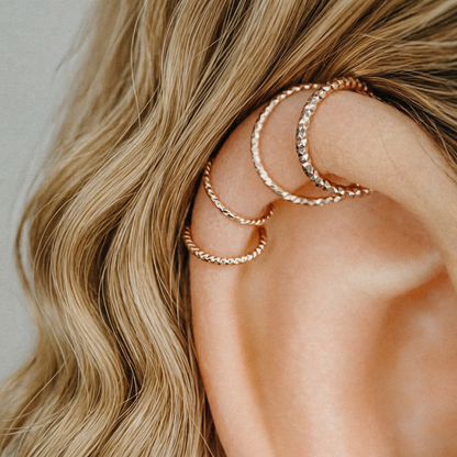 Close-up of three rose gold diamond-cut hoop earrings on a model's helix piercing.
