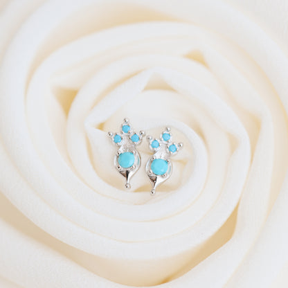 Dainty turquoise earrings on white fabric background