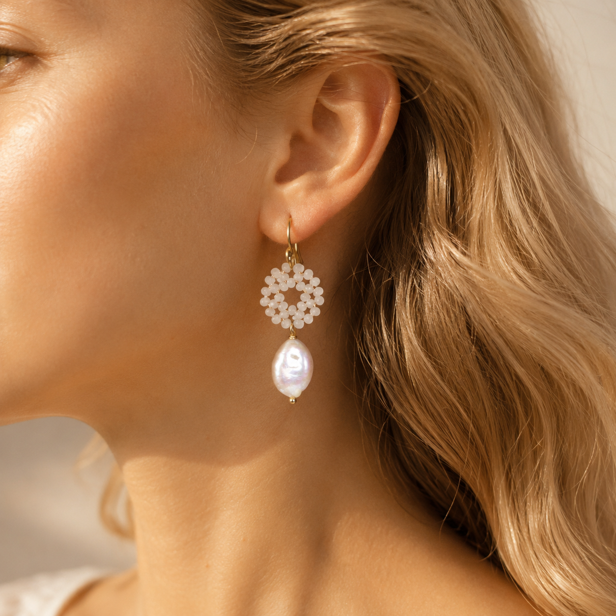 Close-up of a woman wearing a gold-plated baroque pearl drop earring with a delicate white crystal wreath, showcasing its elegant bohemian style.