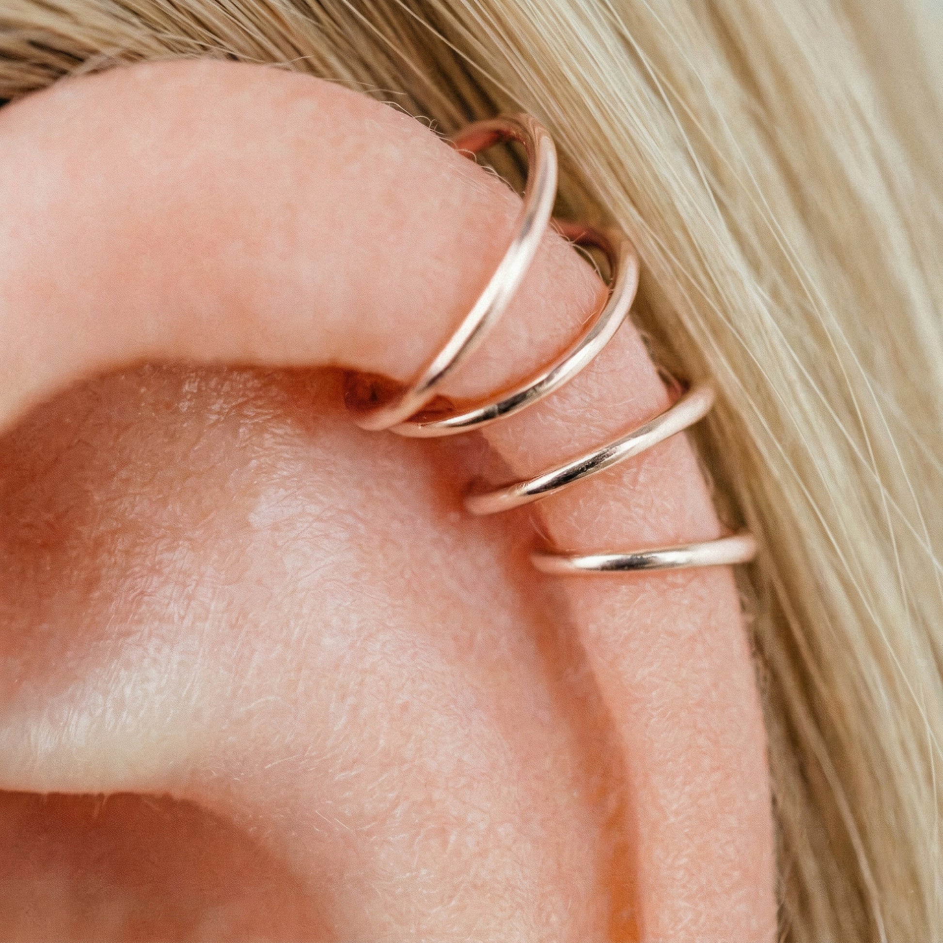 Close-up of a human ear featuring multiple smooth rose gold seamless hoop earrings in various sizes, including helix, tragus, and lobe piercings.