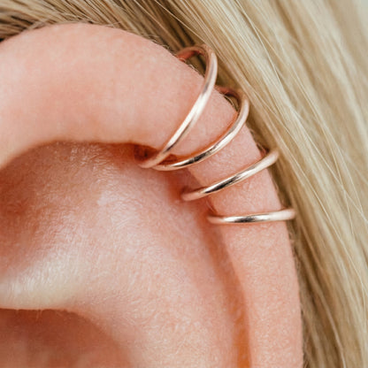 Close-up of a human ear featuring multiple smooth rose gold seamless hoop earrings in various sizes, including helix, tragus, and lobe piercings.