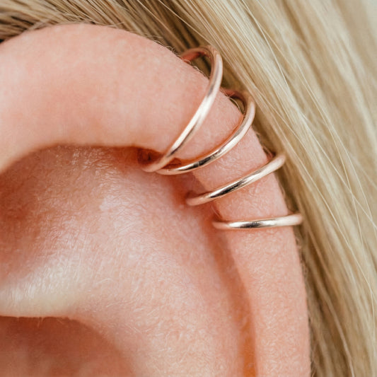 Close-up of a human ear featuring multiple smooth rose gold seamless hoop earrings in various sizes, including helix, tragus, and lobe piercings.