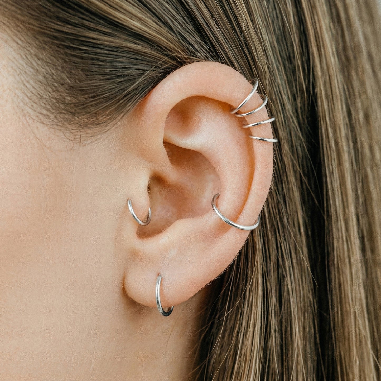 Close-up of a human ear featuring multiple smooth 925 Sterling Silver seamless hoop earrings in various sizes on helix, tragus, and lobe piercings.