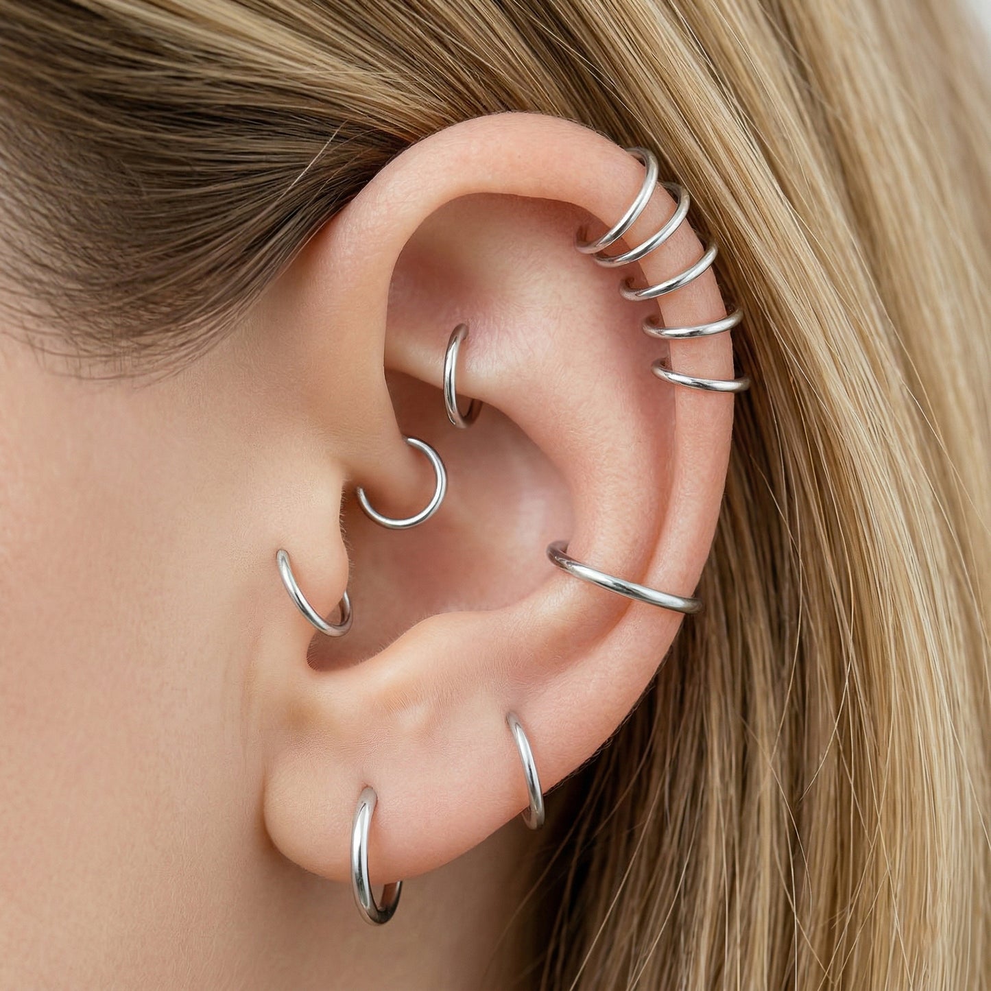 Close-up of a human ear featuring multiple smooth 925 Sterling Silver seamless hoop earrings in various sizes on helix, tragus, and lobe piercings.