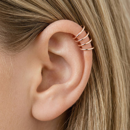 Close-up of a human ear featuring multiple smooth rose gold seamless hoop earrings in various sizes, including helix, tragus, and lobe piercings.