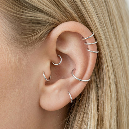 Close-up of a human ear featuring multiple smooth 925 Sterling Silver seamless hoop earrings in various sizes on helix, tragus, and lobe piercings.
