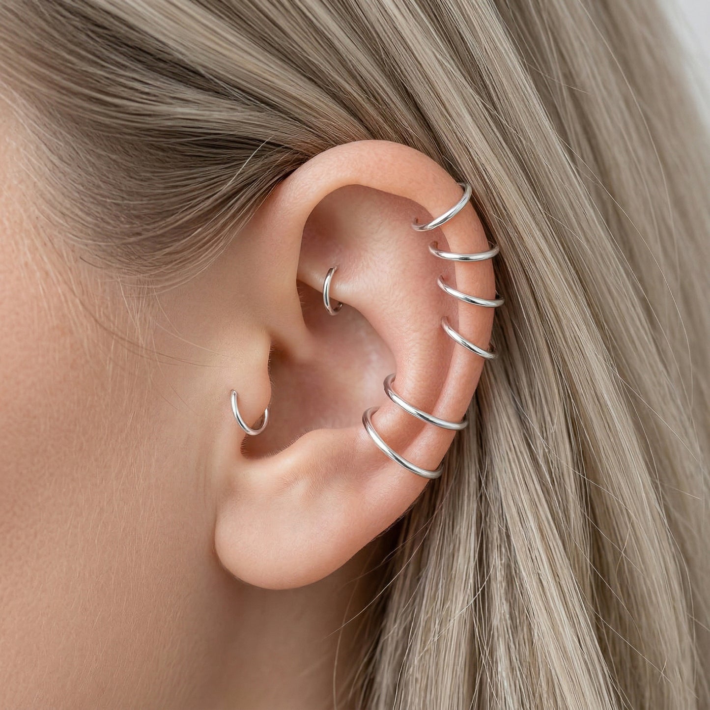 Close-up of a human ear featuring multiple smooth 925 Sterling Silver seamless hoop earrings in various sizes on helix, tragus, and lobe piercings.