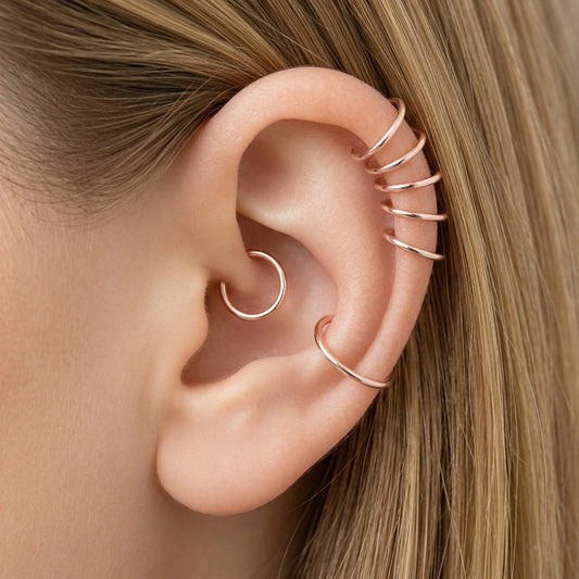 Close-up of a human ear featuring multiple smooth rose gold seamless hoop earrings in various sizes, including helix, tragus, and lobe piercings.