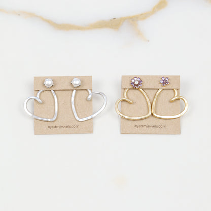 Handmade open heart Ear Jacket earrings designed to sit behind the pierced earlobe beneath an interchangeable stud, available as one Ear Jacket or a matching pair in gold or silver hammered aluminum, approximately 25 mm in diameter, with one coordinating pair of stainless steel post stud earrings included with each order; stud designs vary according to current availability and those shown in the photos are styling examples rather than guaranteed designs.