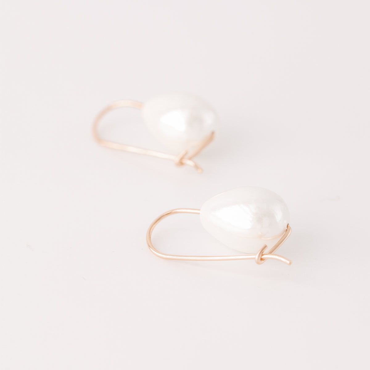 Handmade ceramic pearl teardrop earrings featuring large white pear-shaped pearls approximately 20 mm x 15 mm suspended from a minimalist curved wire hook, approximately 30 mm total length, available in solid 925 sterling silver, 14k gold filled or 14k rose gold filled.