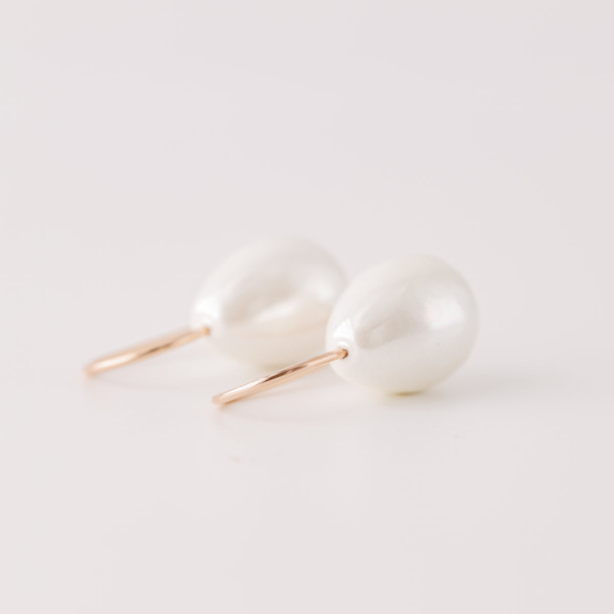 Handmade ceramic pearl teardrop earrings featuring large white pear-shaped pearls approximately 20 mm x 15 mm suspended from a minimalist curved wire hook, approximately 30 mm total length, available in solid 925 sterling silver, 14k gold filled or 14k rose gold filled.