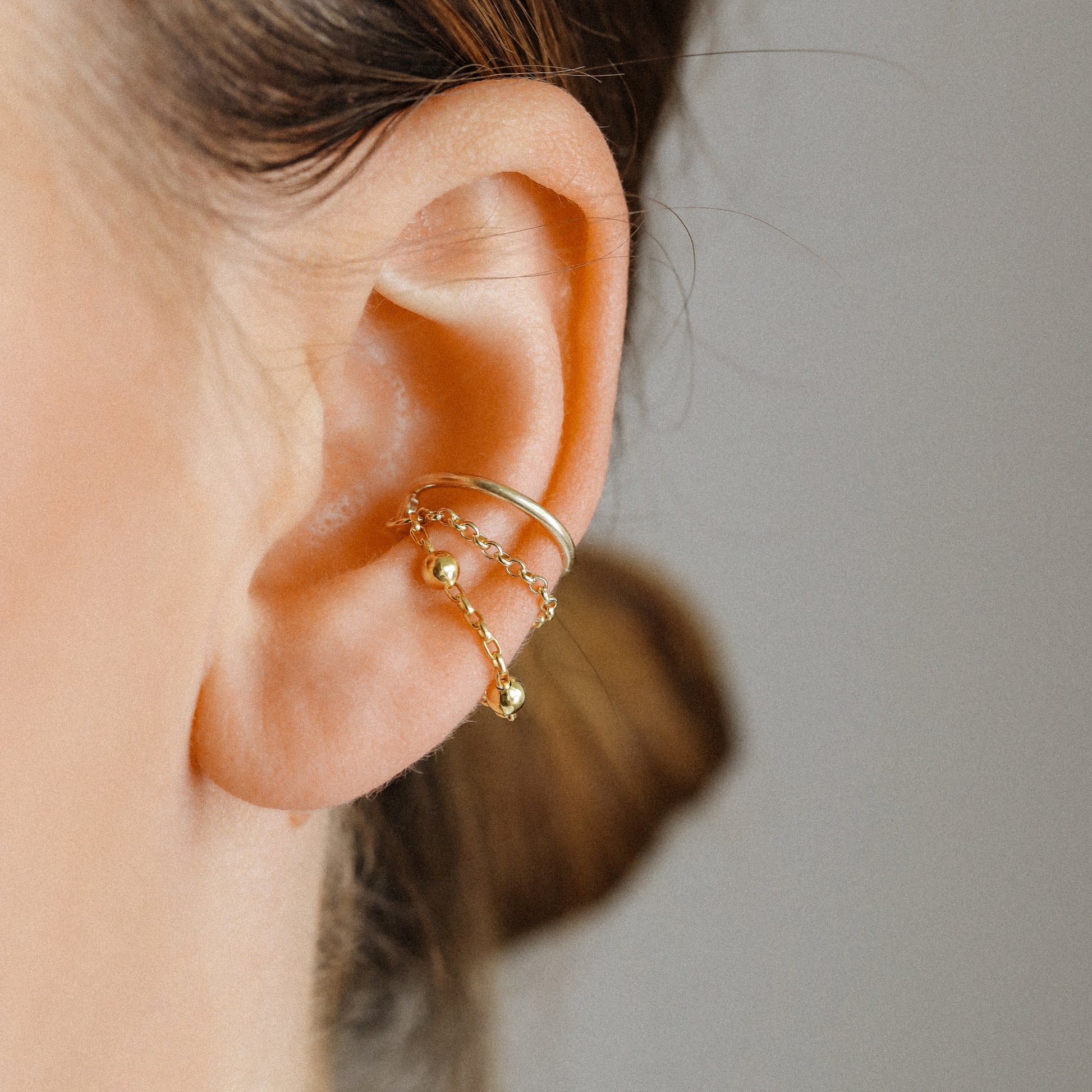 Gold beaded chain ear cuff held close up showing wrap closure and layered chain detail