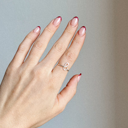 Close-up of a handmade 925 sterling silver wire ring shaped into the letter L on a woman's finger with red French tip nails.