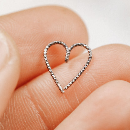 Close-up of a black diamond-cut heart hoop earring held between fingers, showing the textured ruthenium finish on 925 sterling silver.