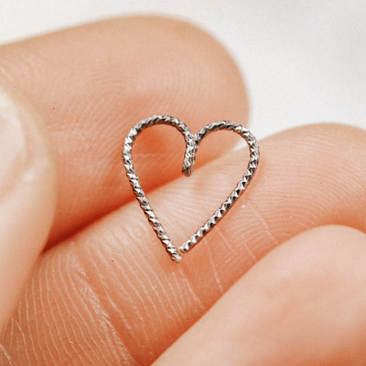 Close-up of a black diamond-cut heart hoop earring held between fingers, showing the textured ruthenium finish on 925 sterling silver.