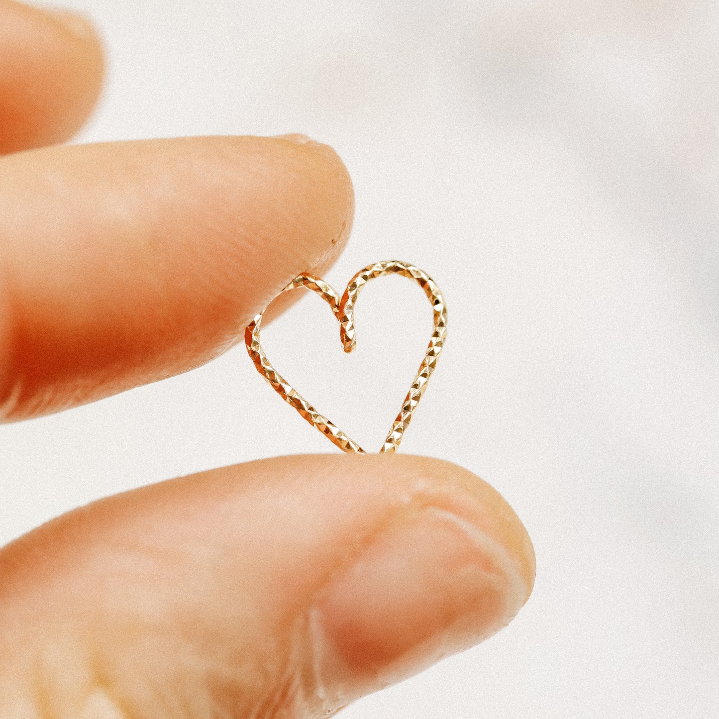 Hand holding a tiny 18k gold heart earring to show scale and delicate craftsmanship.