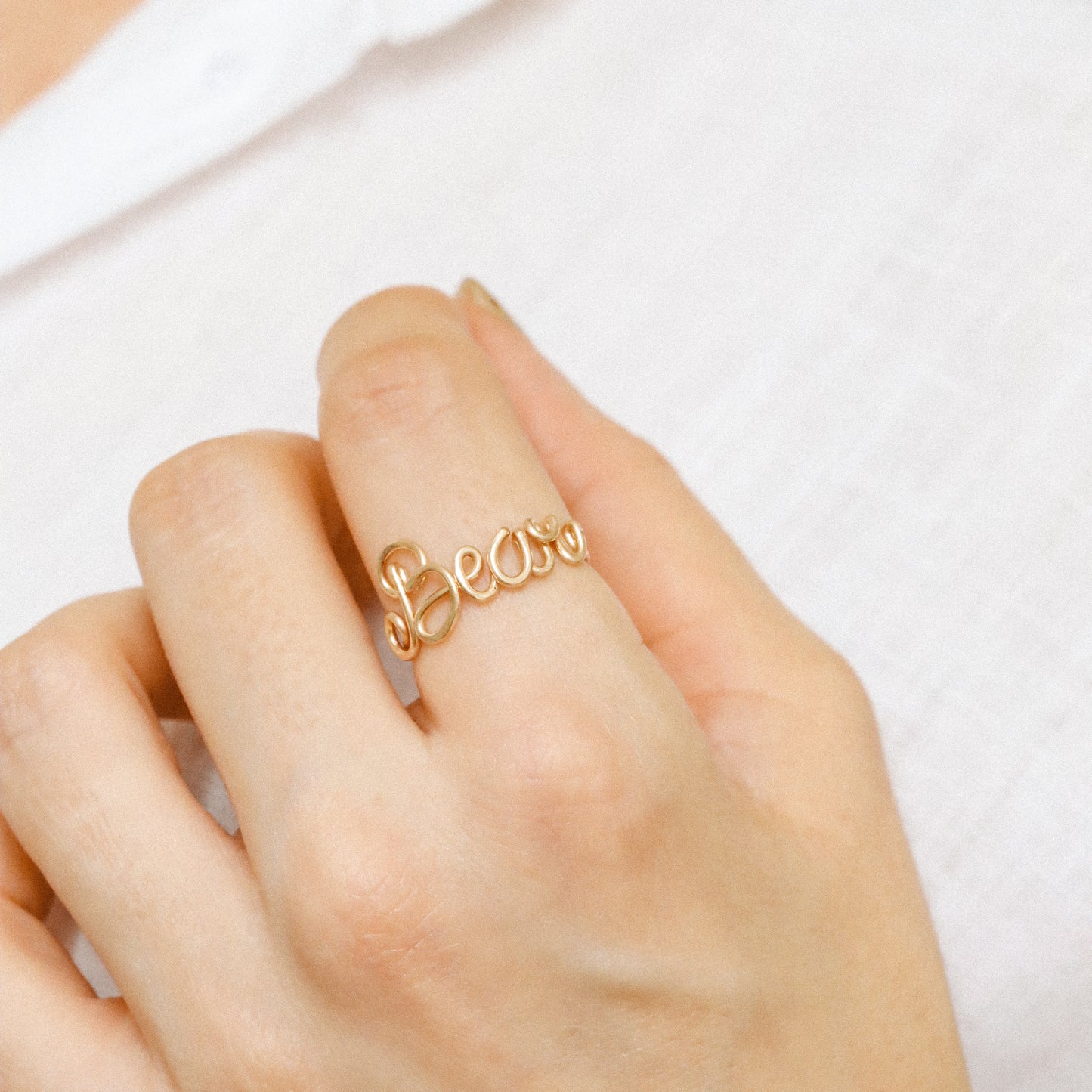 Personalised cursive wire ring in gold with the name "Bear" worn on a hand.
