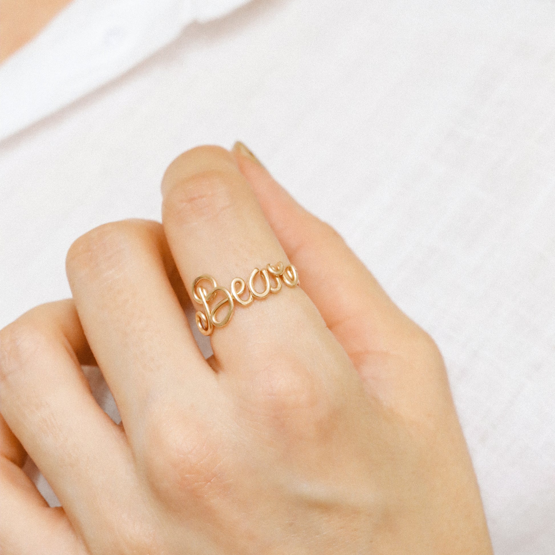 Personalised cursive wire ring in gold with the name "Bear" worn on a hand.