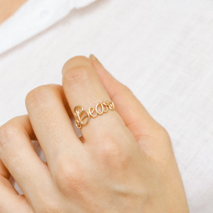 Personalised cursive wire ring in gold with the name "Bear" worn on a hand.