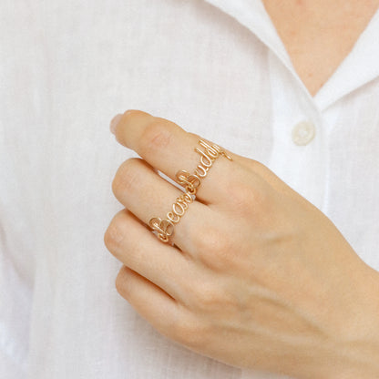 Stacking look featuring multiple handmade gold name rings like "Bear" and "Buddy".