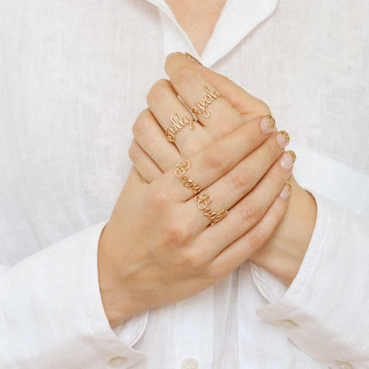 Stacking look featuring multiple handmade gold name rings like "Sully", "Yeah", "Bear", and "Buddy".