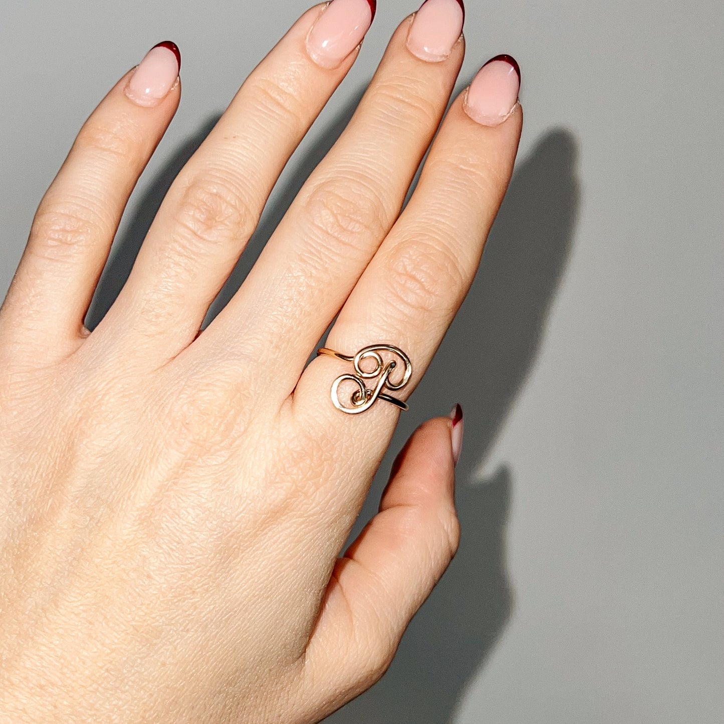 Handmade dainty gold wire ring featuring an uppercase cursive letter P, styled on a hand with red french tip nails.