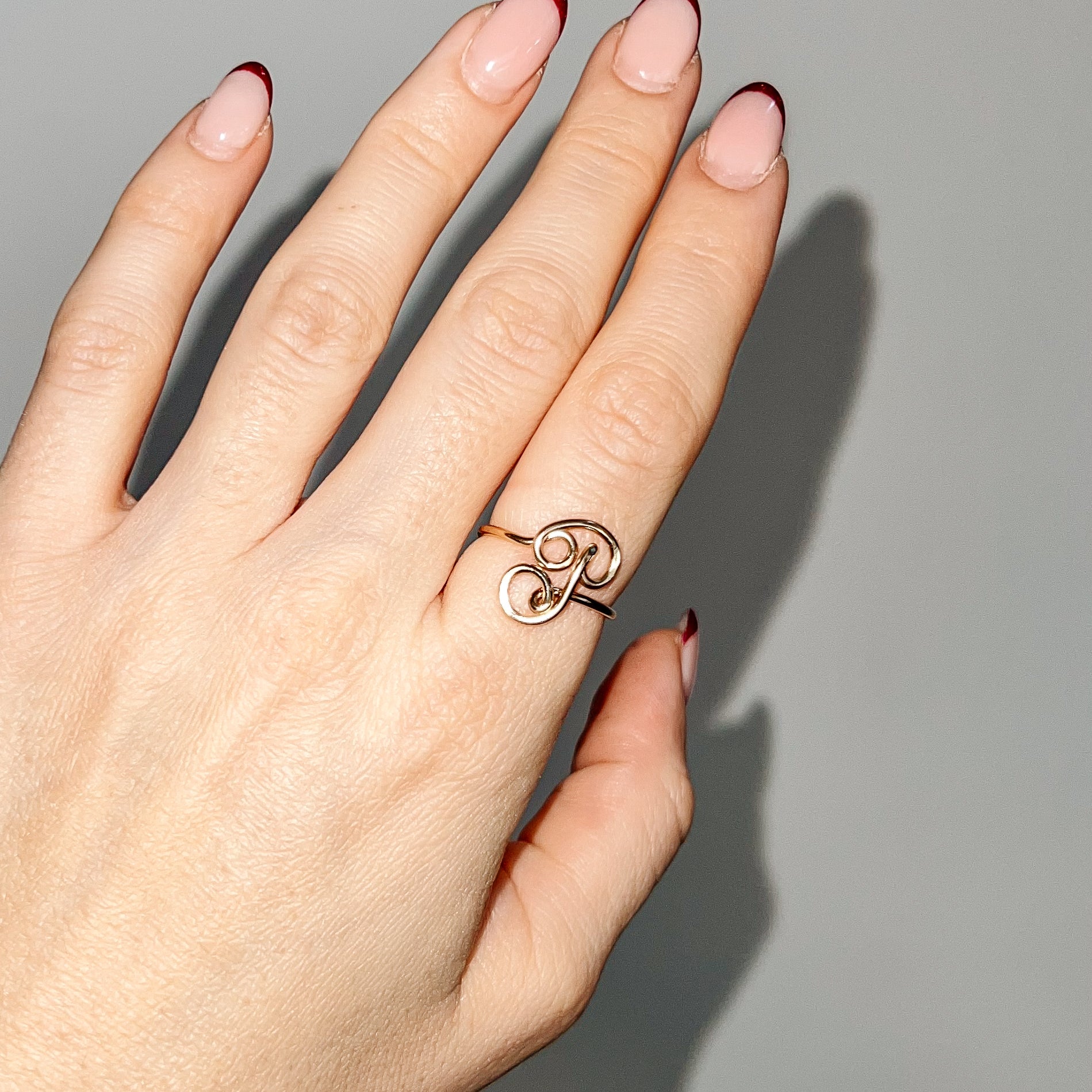 Handmade dainty gold wire ring featuring an uppercase cursive letter P, styled on a hand with red french tip nails.
