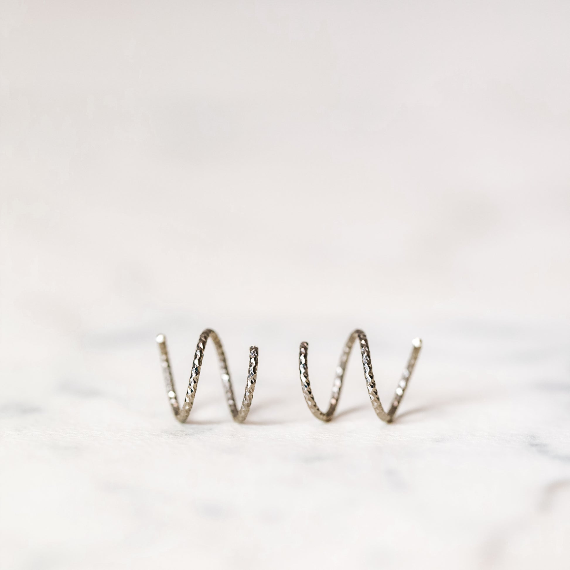 Minimal black double hoop spiral earrings worn on ear, tiny ruthenium sterling silver illusion hoops creating double piercing look, diamond cut texture close-up